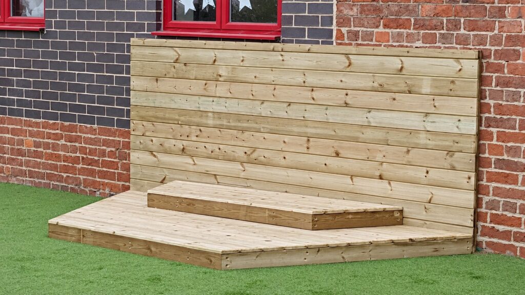 Low timber performance stage with a horizontal-board backdrop beside a school building